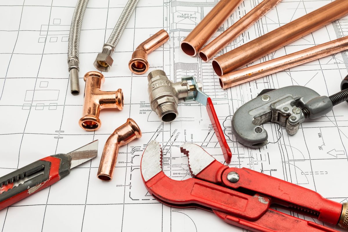 Copper pipes, fittings and a pipe wrench laid out on plumbing plans