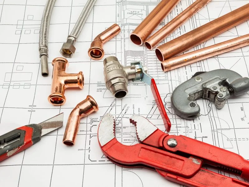 Copper pipes, fittings and a pipe wrench laid out on plumbing plans