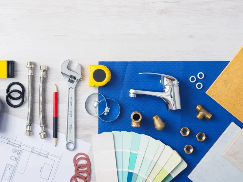 Plumbing fittings, tap, tiles and colour swatches laid out on renovation plans